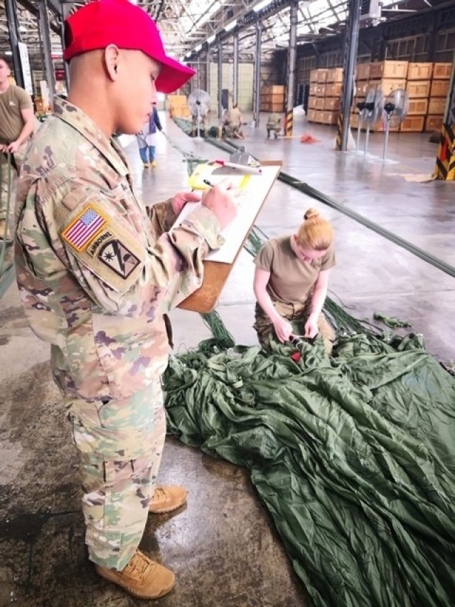 Staff Sgt. Angelito Froa, in-process inspector, observes Spc. Kylie Nielsen as she installs an M-21 reefing line cutter on a G-11 Cargo Parachute System. Both are from the 4th Quartermaster Theater Aerial Delivery Company. (Photo by Chief Warrant Officer 4 Brian Perinon, Japan Support Team, AFSBn-NEA)