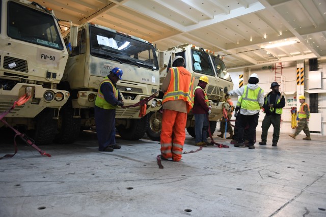 Cooper/Ports America contract workers secure military vehicles on board the Liberty Passion at Naval Weapons Station, Joint Base Charleston in Support of DEFENDER-Europe 20 March 10, 2020. DEFENDER-Europe 20 exercises the deployment of a division-size combat-credible force from the United States to Europe, the drawing of equipment and the movement of personnel and equipment across the theater to various training areas. 