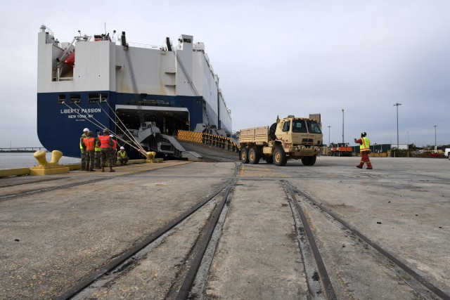 A contract worker directs a vehicle as it its backed onto the M/V Liberty Passion at Naval Weapons Station, Joint Base Charleston in Support of DEFENDER-Europe 20 March 10, 2020. DEFENDER-Europe 20 will exercise the deployment of a division-size combat-credible force from the United States to Europe, the drawing of equipment and the movement of personnel and equipment across the theater to various training areas. 