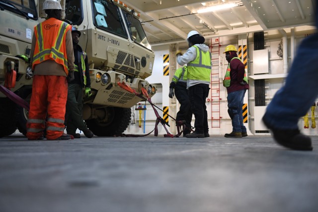 Cooper/Ports America contract workers secure military vehicles on board the Liberty Passion at Naval Weapons Station, Joint Base Charleston in Support of DEFENDER-Europe 20 March 10, 2020. DEFENDER-Europe 20 exercises the deployment of a division-size combat-credible force from the United States to Europe, the drawing of equipment and the movement of personnel and equipment across the theater to various training areas. 