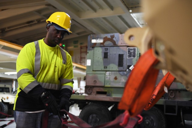 A Cooper/Ports America contract worker secures a military vehicle on board the Liberty Passion at Naval Weapons Station, Joint Base Charleston in Support of DEFENDER-Europe 20 March 10, 2020. DEFENDER-Europe 20 exercises the deployment of a division-size combat-credible force from the United States to Europe, the drawing of equipment and the movement of personnel and equipment across the theater to various training areas. 