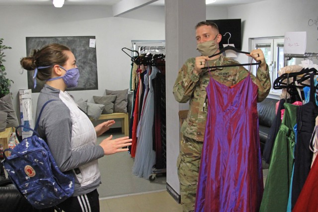 U.S. Army Sgt. Robert Cooper, a crypto linguist with the 24th Military Intelligence Battalion displays a prom dress to Hannah Nuemann, a Wiesbaden High School student during Operation Deploy The Prom on May 16 at the Club Beyond Youth Chapel on U.S. Army Garrison Wiesbaden Hainerberg. Cooper and his wife, Sam Cooper, orchestrated the program Operation Deploy the Prom which gave free ties and dresses to Wiesbaden High School students. (U.S. Army photo by Pfc. Raekwon Jenkins)