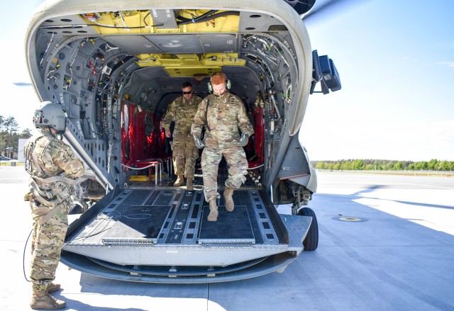 Left, Spc. Justin Cole, B. Co. 1st Bn. 214th Avn. Reg. CH-47 Chinook helicopter crew chief, observes Col. John Broam, 12th Combat Aviation Brigade commander, as he disembarks the helicopter in Grafenwoehr, Germany, with Brig. Gen. Christopher R. Norrie, commanding general, 7th Army Training Command. The exercise was an opportunity for the 1-3rd ARB, to conduct a training mission May 19, with the full battalion under realistic conditions.