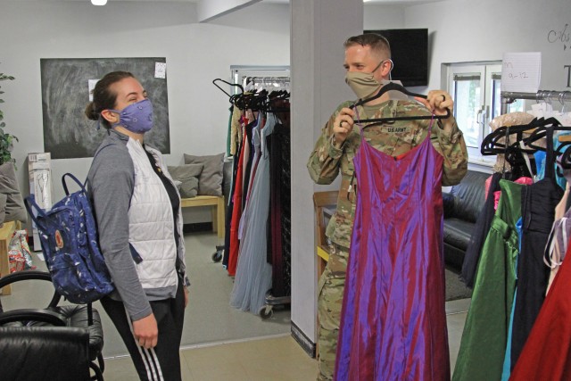 U.S. Army Sgt. Robert Cooper, a crypto linguist with the 24th Military Intelligence Battalion displays a prom dress to Hannah Nuemann, a Wiesbaden High School student during Operation Deploy The Prom on May 16 at the Club Beyond Youth Chapel on U.S. Army Garrison Wiesbaden Hainerberg. Cooper and his wife, Sam Cooper, orchestrated the program Operation Deploy the Prom which gave free ties and dresses to Wiesbaden High School students. (U.S. Army photo by Pfc. Raekwon Jenkins)