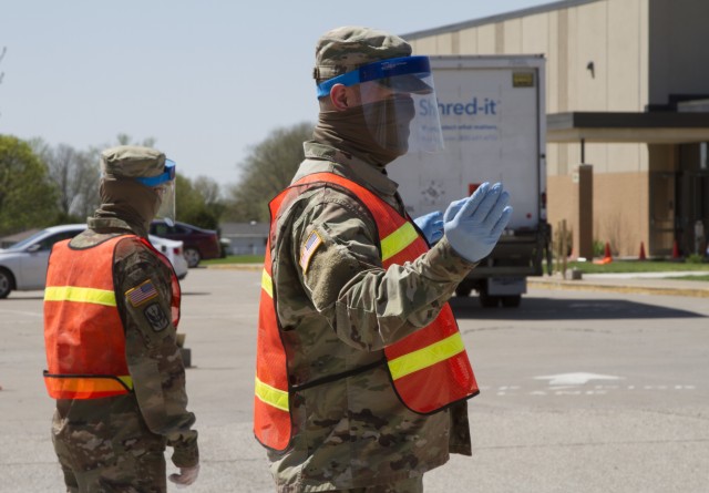 Spc. Colton Fenton and Spc. Kellen Korf with Headquarters and Headquarters Company, 248th Aviation Support Battalion, Iowa Army National Guard, operate a traffic control checkpoint at a two-day, pop-up COVID-19 testing site at West Middle School in Muscatine, Iowa, on April 30, 2020.  More than 46,000 National Guard troops have been called to assist their state in response to the COVID-19 pandemic, and many are now eligible for financial assistance from Army Emergency Relief.