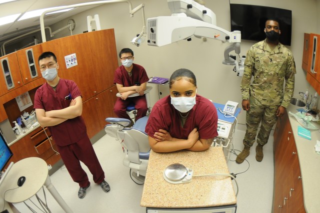 (FROM LEFT TO RIGHT) Spc. Junghyun Lee, Spc. Xingyu Chen, Spc. Renee Gill and Spc. Darius Ballard -- all Col. Bull Dental Clinic dental assistants -- pose amid the backdrop of dental equipment recently. The four are among the 10 enlisted Soldiers and officers who have continued the dental mission here following stay-at-home orders for more than 30 civilian employees at CBDC due to coronavirus concerns.