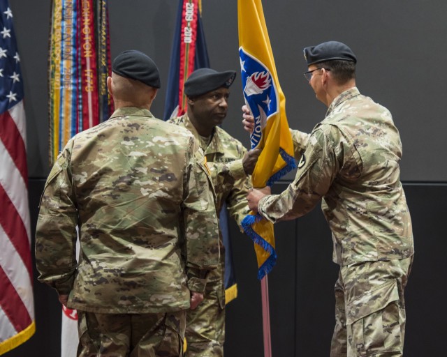 Command Sgt. Maj. Gene Canada, U.S. Army Security Assistance Command's command sergeant major, passes the colors to Maj. Gen. Jeffrey Drushal, outgoing commander, during a relinquishment of command ceremony, 2 June 2020, at Redstone Arsenal, AL. Dr. Myra  Gray, off-screen, USASAC's Senior Executive Service officer and  deputy to the commanding general, will assume 
Executive Director duties.  Lt. Gen. Edward Daly, center with back to camera, the deputy commanding general of Army Materiel Command, hosted the virtual event to a socially distanced audience with widespread online presence live-streamed through social media. (Photo by Richard Bumgardner, USASAC Public Affairs)