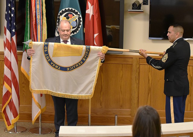 Command Sgt. Maj. Marco Torres, U.S. Army Sustainment Command, unfolds the Senior Executive Service flag presented to Dan Reilly during his SES promotion ceremony at Rock Island Arsenal, Illinois, June 4.