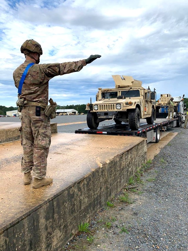 A Soldier with the 4th Security Force Assistance Brigade gives hand and arm signals to a fellow Soldier while donning a mask for COVID-19 mitigation during vehicle off-loading operations at the centralized receiving and shipping point (CRSP) on...