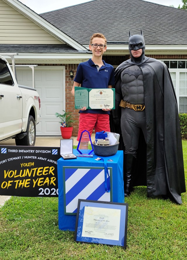Preston Ver Hoef, the Fort Stewart Hunter Army Airfield’s 2020 youth volunteer of the year award winner poses with Sgt. Anthony Licata, a trumpet player assigned to the 3rd Infantry Division Band who is dressed as Batman, while holding his public service commendation medal, June 4, 2020, at his residence in Richmond Hill, Georgia. “Batman” presented Ver Hoef the award for over 60 hours of community service through Richmond Hill Middle School by offering support to special needs students. (U.S. Army photo by Sgt. Arjenis Nunez)