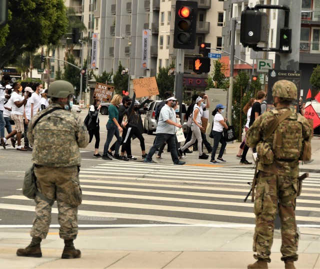 Cal Guardsmen are posted on a street corner in downtown Los Angeles as protestors march past them on June 5, 2020. By this time, protests in Los Angeles were no longer violent or causing the destruction of property. (U.S. Army photo by Capt. Jason...