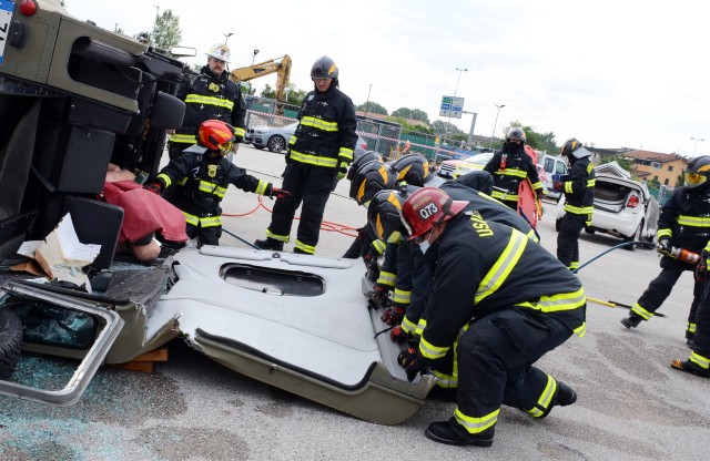 Firefighters from U.S. Army Garrison Italy Emergency Services directorate lay down the roof of the vehicle to allow for safe removal of the trapped passenger, under the watchful eyes of evaluators.