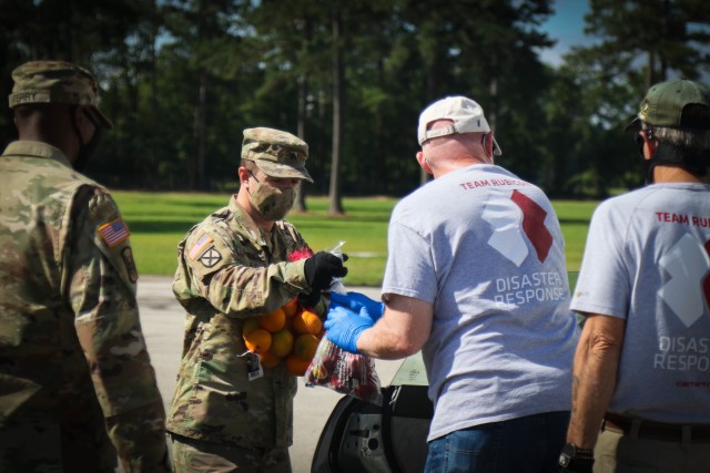 North Carolina Army National Guard Sgt. Timothy Cornell (left), assigned to 2-130th Airfield Operations Battalion, hands a bag of produce to Mark Heinlein, a volunteer for Team Rubicon, a veteran disaster relief service organization, during the Second Harvest Food Bank Southeast food distribution at the Midway Elementary School in Dunn, N.C., June 18, 2020. The NCNG is working with North Carolina Emergency Management, N.C. Department of Health and Human Services and local food banks to help support COVID-19 relief efforts. (North Carolina Army National Guard photo by Spc. Hannah Tarkelly, 382nd Public Affairs Detachment/Released).