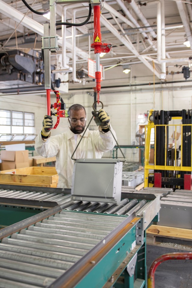 Steve Meadows lifts a reactive armor tile onto a conveyor belt as it is prepared for painting at Anniston Munitions Center.