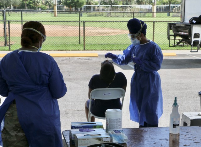 Spc. Leticia Bates, a Soldier with the 2-265th Air Defense Artillery Battalion, waits for a nurse to finish performing a nasal swab to assist with the specimen collection at the Vincent Torres Memorial Park Community Based Testing Site in Lauderdale Lakes, Broward County. The Lauderdale Lakes CBTS is one of two new CBTS locations in Broward that opened recently. (U.S. Army National Guard photo by Maj. Jesse Manzano.)