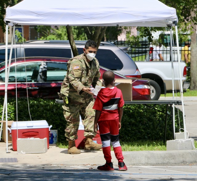 Pfc Talal Rawashdesh, a Soldier with A Company, 2-124th Infantry Battalion, hands out water to a minor outside the Lincoln Park Community Based Testing Site (CBTS) in Fort Lauderdale, Broward County. The Lincoln Park CBTS is one of two new CBTS...