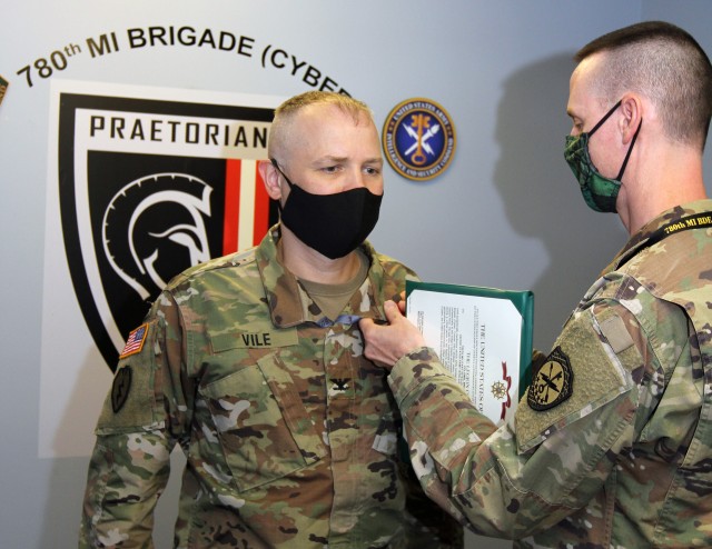 FORT GEORGE G. MEADE, Md. -- Col. Brian D. Vile (left) receives the Legion of Merit for his service as the commander of the 780th Military Intelligence Brigade (Cyber) from Command Sgt. Maj. Ronald Krause, the brigade’s senior enlisted leader, in the brigade headquarters, July 1. Vile will relinquish his command to Col. Matthew J. Lennox in a virtual change of command ceremony hosted by Maj. Gen. Gary W. Johnston, commanding general, U.S. Army Intelligence and Security Command (INSCOM), on July 2. To watch the full video of the virtual change of command ceremony visit the 780th MI Brigade Facebook page at https://www.facebook.com/780MIBDE/.