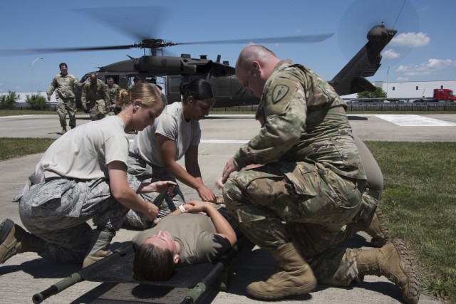 Airmen and Soldiers from the Indiana National Guard prepare to load a patient into a UH-60 Black Hawk helicopter during a medical transport exercise at the Johnson County Armory, Franklin, July 2, 2020. During the exercise, members practiced loading and unloading procedures via voice direction with the aircraft off and using hand signals with the aircraft engines running. Due to rotor wash, aka propeller wash, service members did not wear masks for safety reasons as the masks could cause debris interfering with helicopter propellers. (U.S. Air National Guard photo by Staff Sgt. Justin Andras)