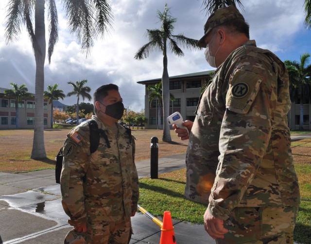 Sgt. 1st Class Povilas Pultinevicius, 4960th Multi-Functional Training Brigade Operations Non-Commissioned Officer-In-Charge, checks the temperature of a student entering the schoolhouse at Fort Shafter Flats, Honolulu, Hawaii July 17th, 2020, adhering to the schoolhouse's COVID-19 safety measures and procedures.