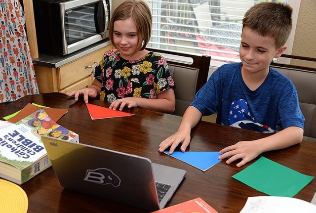 Nine-year-old twins Victoria and Timothy Kallo watch instruction, delivered by sportscasters in an online video as if origami were a sport, and fold paper flowers during Vacation Bible School July 21 at their on-post home. Due to ongoing COVID-19...