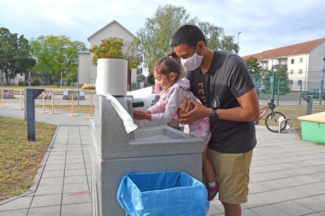 WIESBADEN, Germany - Sgt. Luis Steven Pineda helps daughter Daniella wash her hands before dropping her off at the Child Development Center July 24 on Clay Kaserne. CDCs at U.S. Army Garrison Wiesbaden have implemented safety measures as they...