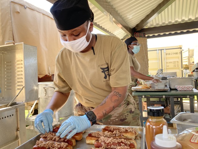 Specialist Keilah Jones, a culinary specialist assigned to 1st Battalion, 187th Infantry Regiment, 3rd Brigade Combat Team, 101st Airborne Division (Air Assault), prepares a pulled pork gourmet hot dog, named the Back Yard Pit Dog, for the Hot Dog...