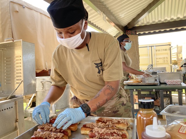 Specialist Keilah Jones, a culinary specialist assigned to 1st Battalion, 187th Infantry Regiment, 3rd Brigade Combat Team, 101st Airborne Division (Air Assault), prepares a pulled pork gourmet hot dog, named the Back Yard Pit Dog, for the Hot Dog Cook-off July 15 between battalions outside the Rak Café using field feeding equipment. The contest also provided a training opportunity for the Soldier-chefs. (Stephanie Ingersoll, Fort Campbell Courier)