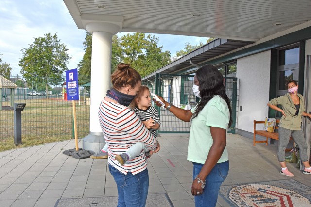 WIESBADEN, Germany - Amanda Campbell holds her daughter, Kate, while Hazel Ann Swan, supervisory program specialist at the Child Development Center, takes her temperature July 24 during morning drop off. CDCs at U.S. Army Garrison Wiesbaden have...