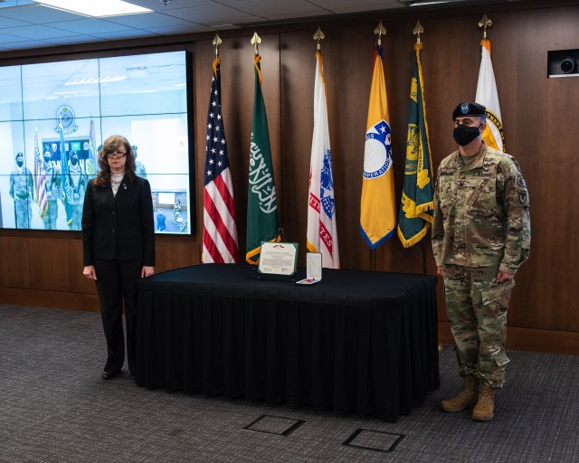 Dr. Myra Gray, left, the Executive Director of U.S. Army Security Assistance Command, prepares to award the Legion of Merit, to outgoing Program Manager for the Office of the Program Manager-Saudi Arabian National Guard Modernization Program, Col. John DiGiambattista, following a Change of Charter ceremony, on July 1, at Redstone Arsenal, AL.  Dr. Gray hosted the event as Col. DiGiambattista, relinquished his duties to Col. John White. On the screen, via video teleconferencing, is the OPM-SANG Honor Guard, located in Riyadh, Saudi Arabia. (US Army photo by Richard Bumgardner)