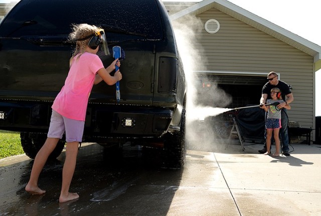 While 8-year-old Isabella VanKirk scrubs the back of her neighbor's vehicle, her father, Lt. Col. Patrick VanKirk, Department of Sustainment and Force Management, Command and General Staff College, and her twin sister, Angelina, use a power washer to rinse the front and side of the SUV July 25 on post. The neighbor offered to pay the twins to wash the vehicle, and the girls said they were going to use the money toward a Lego playset. The Fort Leavenworth Lamp staff provided a glimpse of life on post Saturday on the same day that "Life in a Day" participants were filming glimpses of their lives for the worldwide documentary July 25. Photo by Prudence Siebert/Fort Leavenworth Lamp