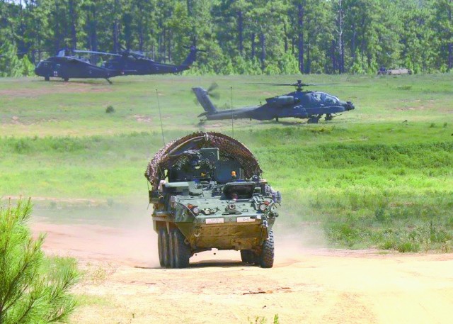 A vehicle traverses the JRTC “Box” while helicopters sit in the background during a recent rotation.