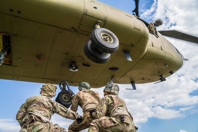 A crew chief with B Co "Big Windy," 1-214th General Support Aviation Battalion relays vital position information back to the CH-47 Chinook pilot from his side window as paratroopers from the 173rd Airborne Brigade prepare to hook their pallet of equipment to the underside of the helicopter. (U.S. Army photo by Maj. Robert Fellingham)