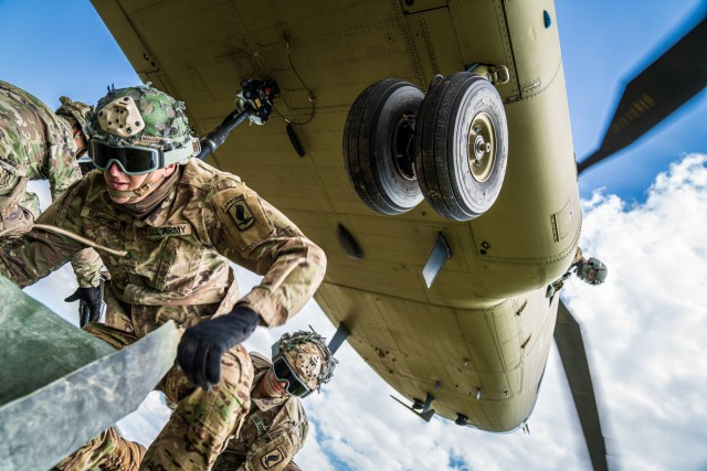 A crew chief with B Co "Big Windy," 1-214th General Support Aviation Battalion relays vital position information back to the CH-47 Chinook pilot from his side window as paratroopers from the 173rd Airborne Brigade hook their pallet of equipment to...