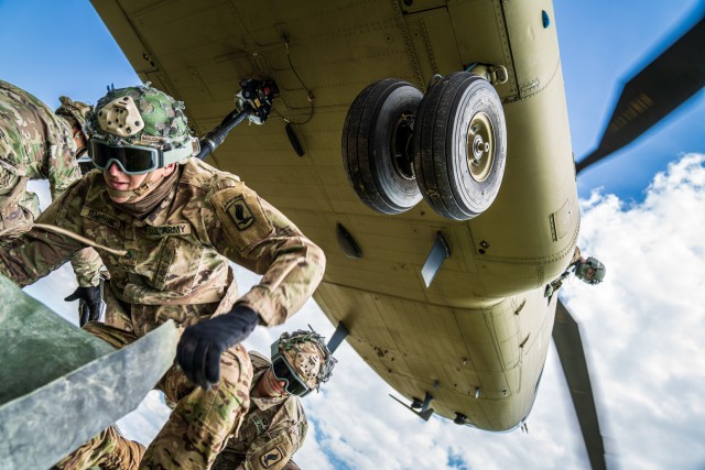 A crew chief with B Co "Big Windy," 1-214th General Support Aviation Battalion relays vital position information back to the CH-47 Chinook pilot from his side window as paratroopers from the 173rd Airborne Brigade hook their pallet of equipment to the underside of the helicopter. (U.S. Army photo by Maj. Robert Fellingham)