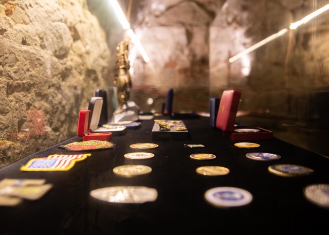 Military coins and decorations sit inside a case in the catacombs of the Saints Peter and Paul Garrison Church in Lviv, Ukraine, Aug. 5.  (Photos by Army Cpl. Shaylin Quaid, JMTG-U Public Affairs)