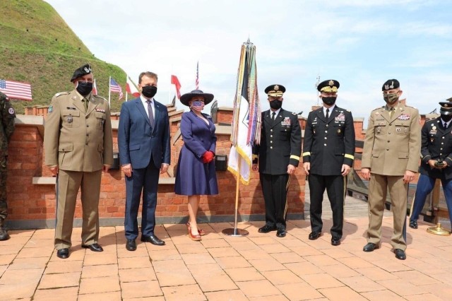 U.S. Army, Polish Ministry of Defense and State Department officials gather around the newly unfurled V Corps flag in Krakow, Poland, Aug. 4. The primary mission of V Corps Headquarters (Forward) will be conducting operational planning, mission command oversight of rotational forces in Europe and will provide additional support to allies and partners in the region.