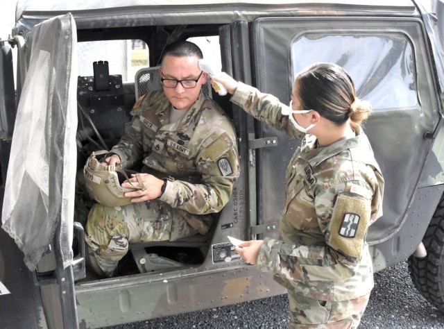 Spc. Stephanie Rivera, 32nd Hospital Center, Fort Polk, checks the temperature of Staff Sgt. Ronny Garza, Joint Readiness Training Center Task Force 2, after she asked him to remove his mask to facilitate the test, before he heads into the Joint...
