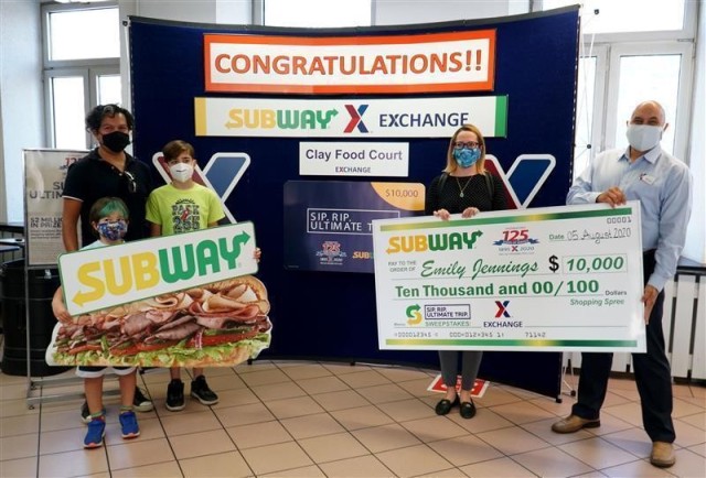 Army & Air Force Exchange Service Wiesbaden General Manager Brian Smith (first on right), presents Emily Jennings with a $10,000 mock check at the Clay Kaserne food court. Jennings won a $10,000 shopping spree courtesy of the Exchange’s Subway...
