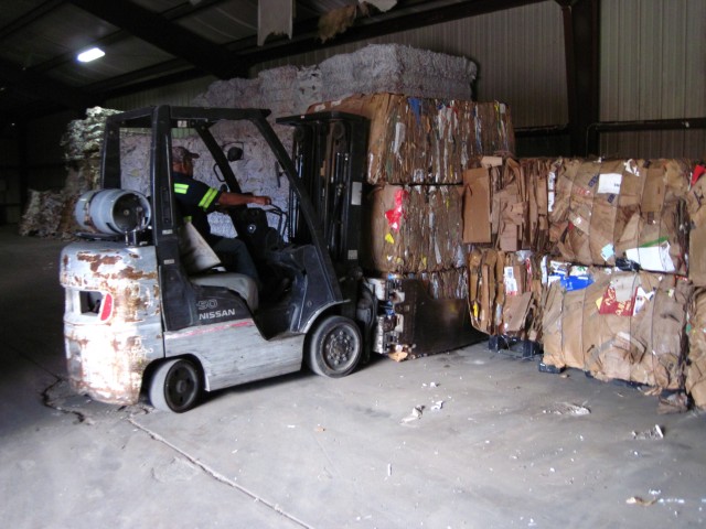 Materials handler Manuel Cruz offloads three additional 1,100-pound bales of corrugated cardboard, transported from the recycle center’s baler in Building 3334 to a staging area in Building 3335 at Fort Sill, Okla. From left to right, staging...