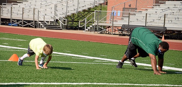 Six-year-old Liam Caffery and Patrick Shelton, Youth Sports and Fitness director, do a bear crawl from one white line to the next during Fitness Camp Aug. 24 at Normandy Field. Photo by Prudence Siebert/Fort Leavenworth Lamp