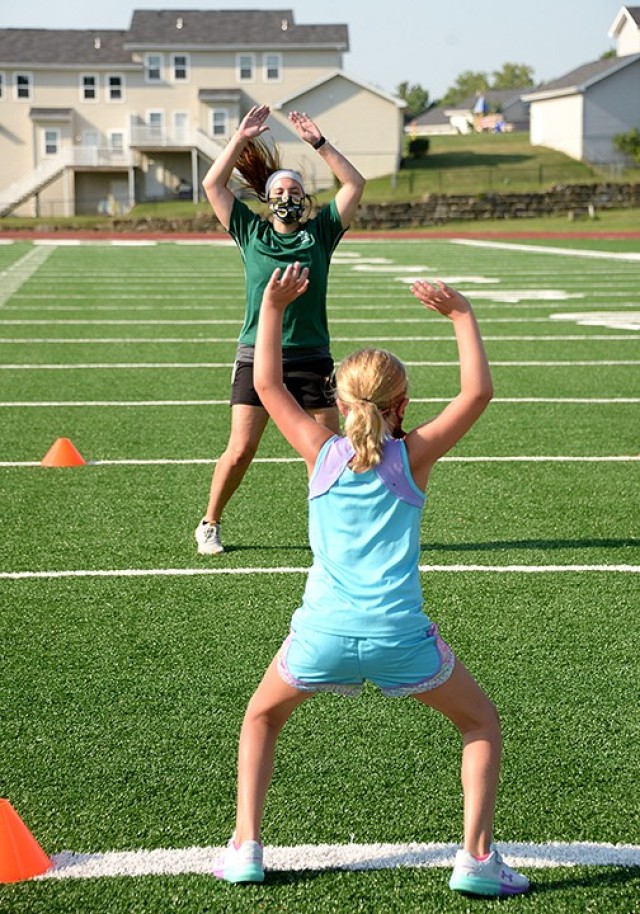 Six-year-old Addilyn Banter and Mallory Barnhouse, Youth Sports and Fitness fitness specialist, do jumping jacks during Fitness Camp Aug. 24 at Normandy Field. Photo by Prudence Siebert/Fort Leavenworth Lamp