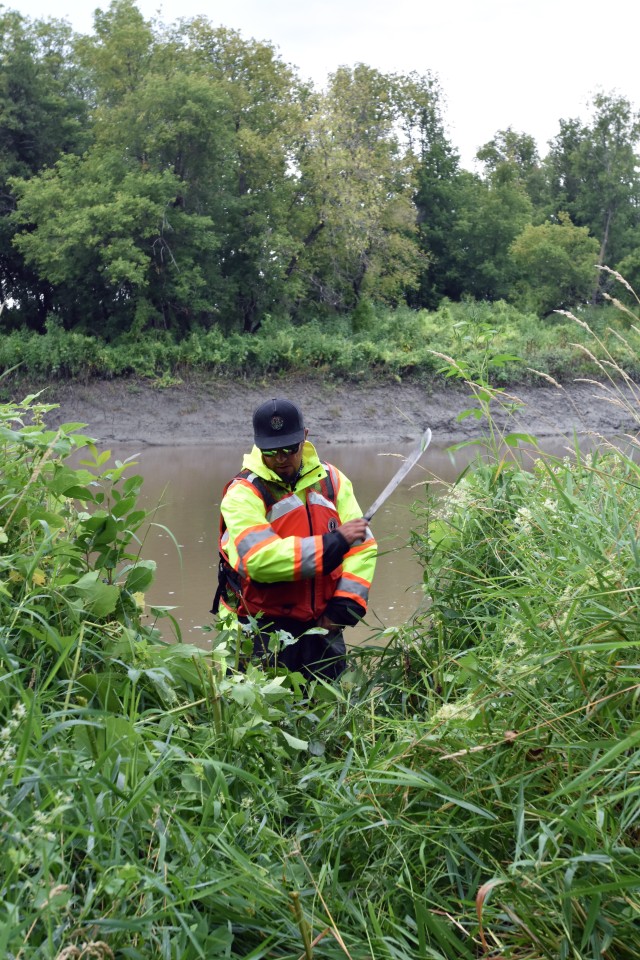 Eduardo Torrens, St. Paul District civil engineer, uses a machete to clear weeds away from a survey monument along the Red River of the North, near Georgetown, Minnesota, Aug. 12. The Corps of Engineers, St. Paul District, in partnership with the Rock Island and Omaha districts and the FM Diversion Authority, are placing monuments to get a better understanding of the environment within the region and to monitor for any potential impacts related to the construction and/or operation of the Fargo – Moorhead Metro Diversion Flood Risk Management Project.