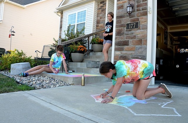 Cassy Ray watches her 12-year-old daughter Shea Ray and Shea’s 12-year-old friend Annabelle Longfellow use sidewalk chalk to create tie-dyed-inspired art in front of the Ray residence during the Beautiful Day in the Neighborhood Meet and Greet...