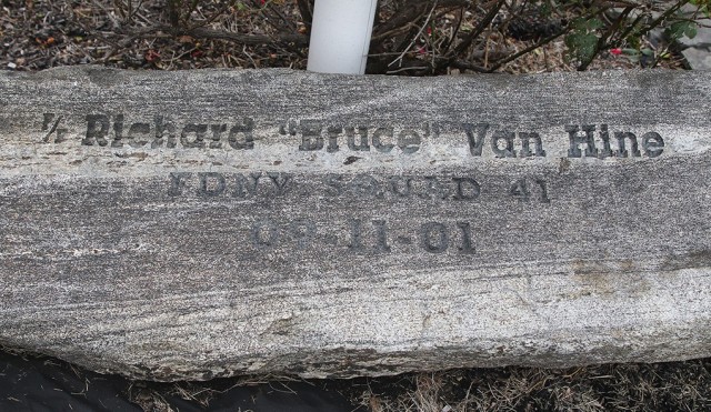 A memorial stone etched with Richard “Bruce” Van Hine’s name, squad and 9/11 date is placed in a well-kempt area with a flowery bush under the flagpole on the fire department's front lawn.