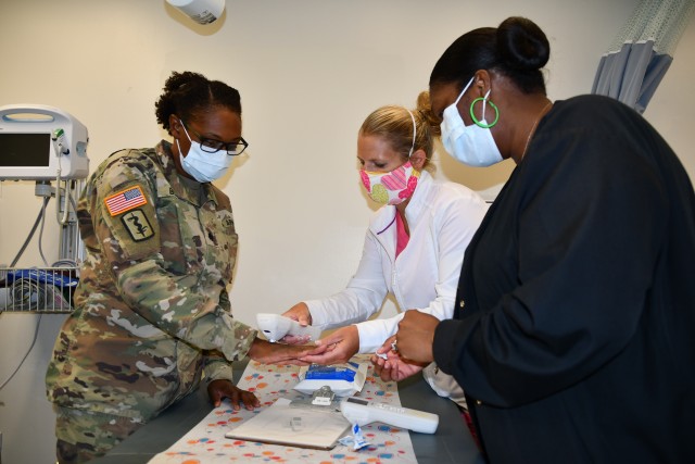 (LEFT) Kenner Army Health Clinic’s staff members; Lt. Col (P) Tameka Bowser, deputy commander for nursing, Bobbie Jo Vohun, registered nurse and Tamika Elliott, license practitioner nurse, both in Wilkerson Pediatrics Clinic discuss how to use the BiliCheck system, which is a non-invasive jaundice assessment device in an exam room in Pediatrics on August 14, 2020.