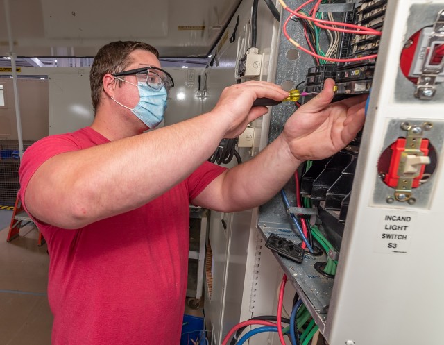 Electrician Travis Burns installs circuit breakers in an Armament Repair Shop Set panel.