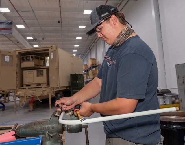 Electrician Helper Stephen Yachwak prepares conduit for installation in an Armament Repair Shop Set shelter.