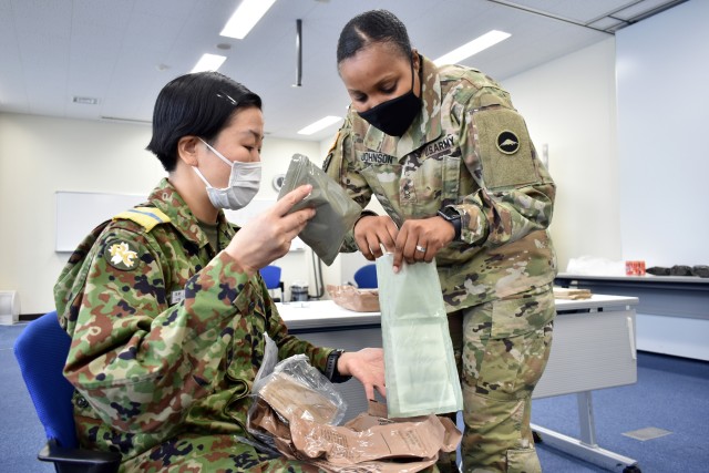 Master Sgt. Shanika Johnson, right, assigned to U.S. Army Reserve Affairs Japan, U.S. Army Japan, helps Ayano Miyakawa, a Japan Ground Self-Defense Force Technical Reserve Candidate, with her Meal, Ready-to-Eat heater during the JGSDF Reserve...