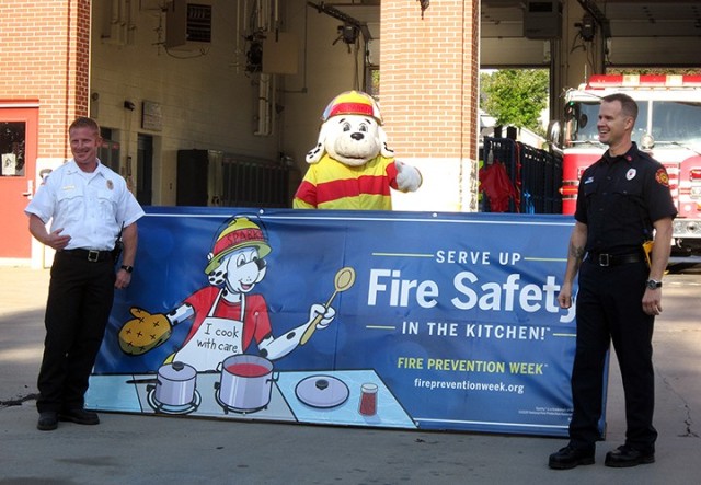 Fort Leavenworth Fire and Emergency Services Battalion Chief Dustin Hensley; Sparky the Fire Dog, portrayed by Fire Inspector Antonio Masisak; and Fire Inspector Aaron Dennis film a Fire Prevention Week video Sept. 25 at Fire Station No. 2. "Serve up fire safety in the kitchen" is the theme of this year's Fire Prevention Week. Photo by Prudence Siebert/Fort Leavenworth Lamp