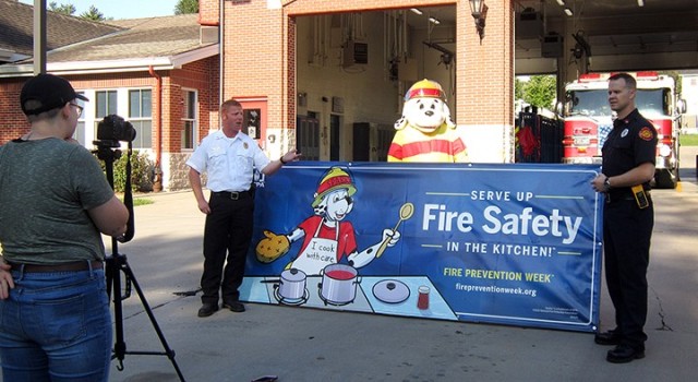 Fort Leavenworth Fire and Emergency Services Battalion Chief Dustin Hensley; Sparky the Fire Dog, portrayed by Fire Inspector Antonio Masisak; and Fire Inspector Aaron Dennis film a Fire Prevention Week video with the help of Annika Kinder, Fort Leavenworth Public Affairs intern and senior at Park University, Sept. 25 at Fire Station No. 2. "Serve up fire safety in the kitchen" is the theme of this year's Fire Prevention Week. Photo by Prudence Siebert/Fort Leavenworth Lamp